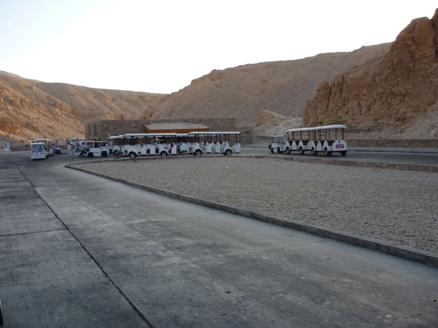 Electric Tuf-tuf trams parked at the visitor centre car park beneath the Theban cliffs