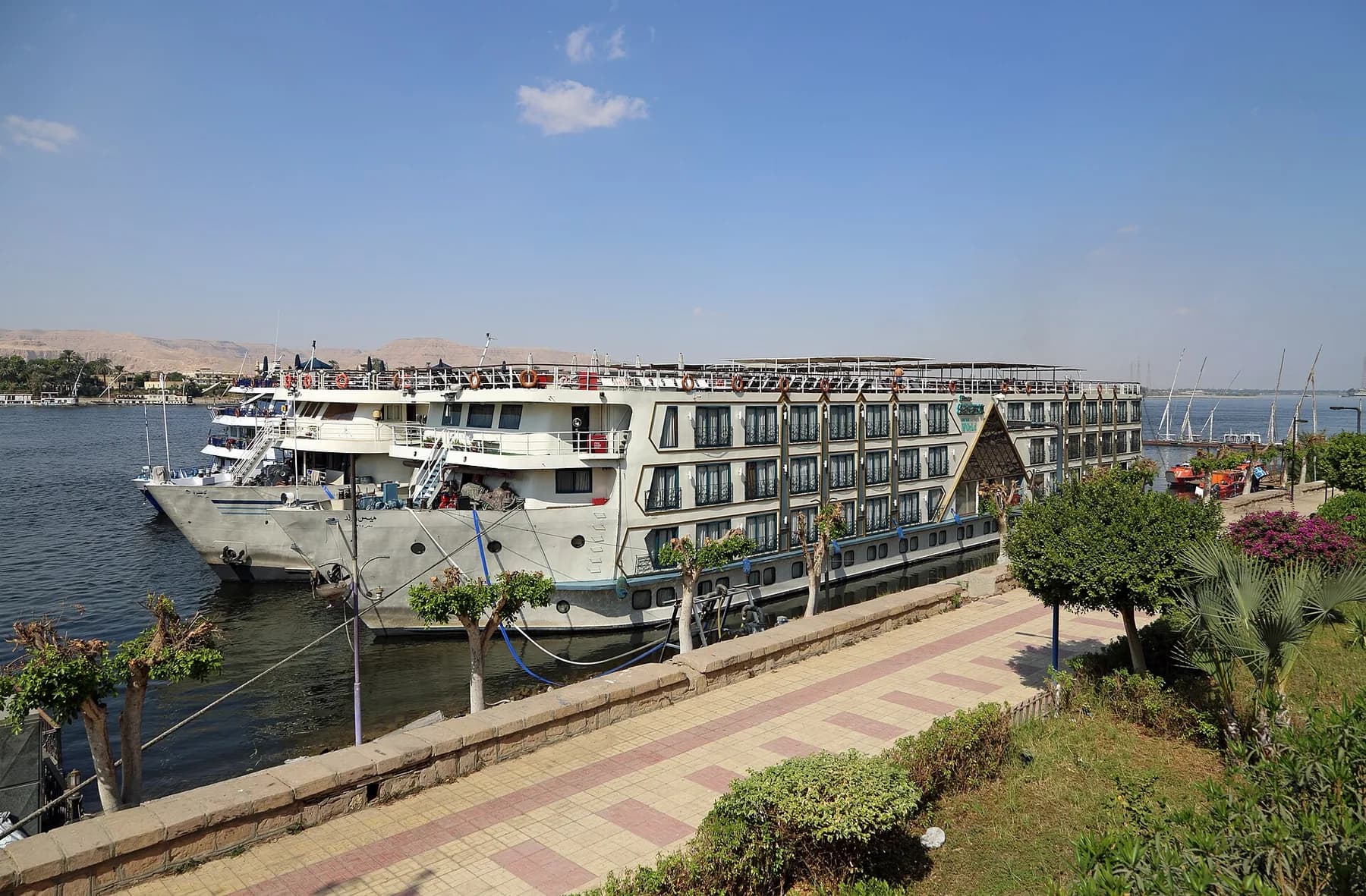 Two cruise ships moored side by side at a landscaped riverside quay