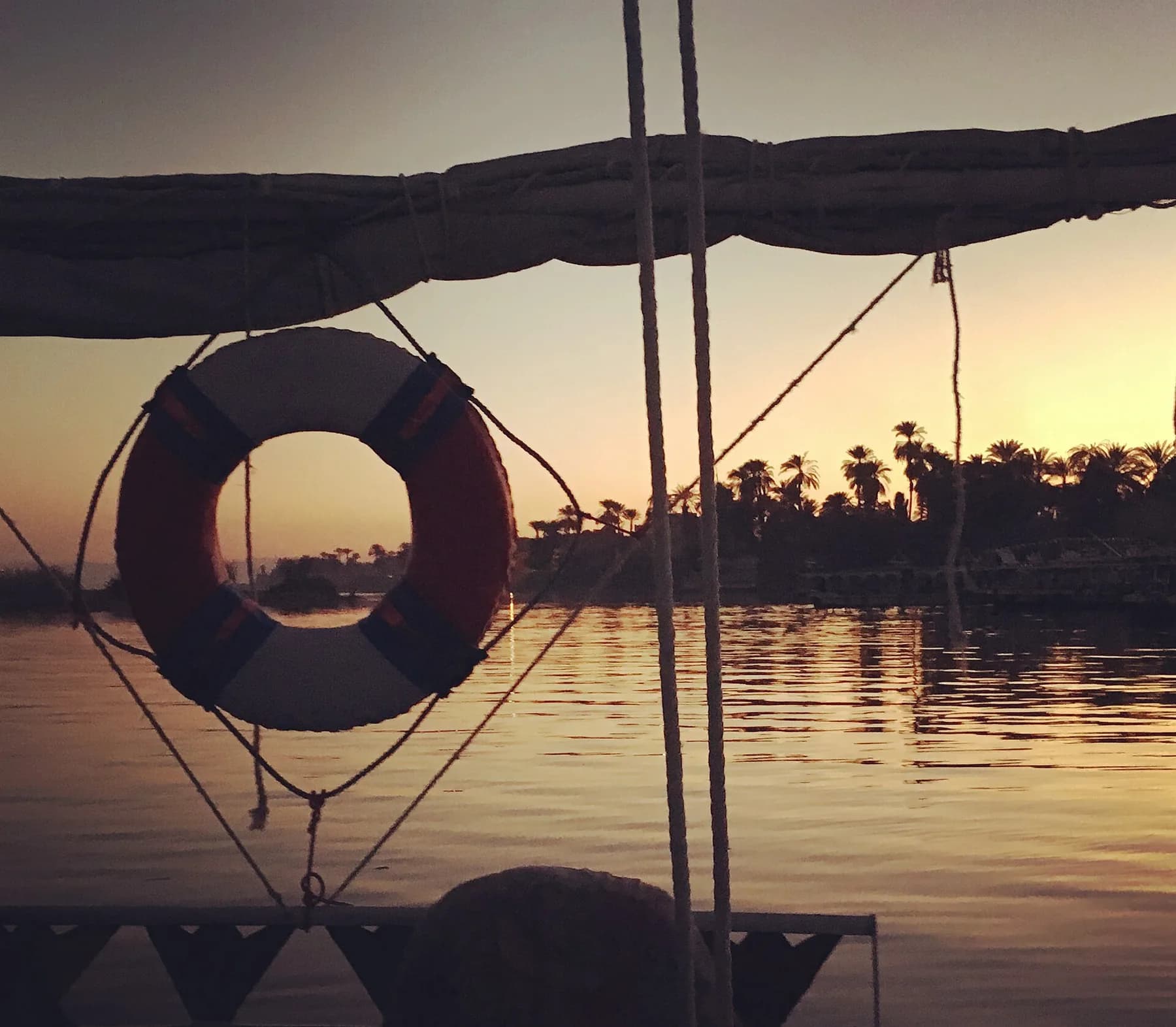 Sunset over the Nile at Luxor framed by a lifebuoy and awning on a boat