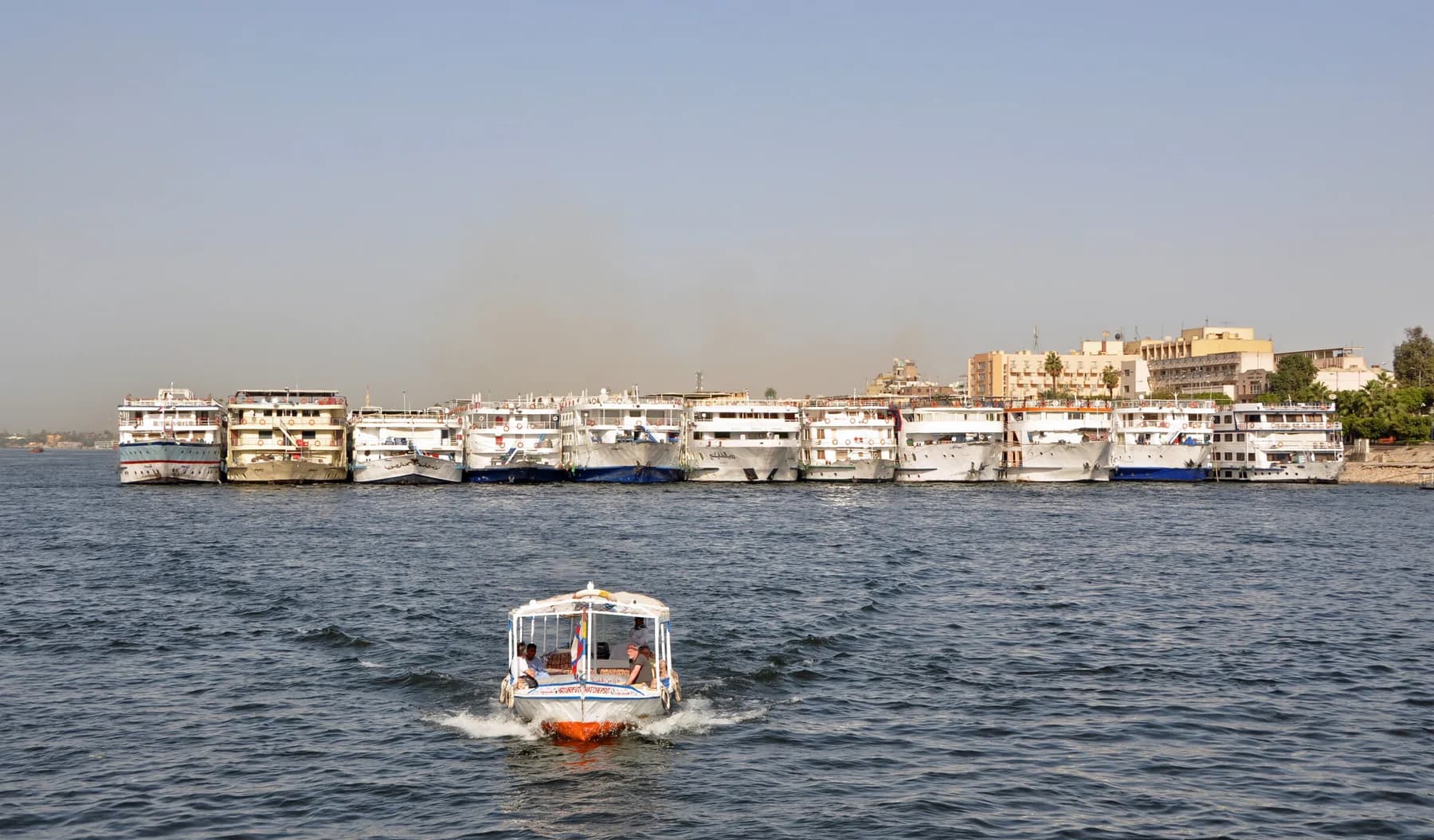 Long line of Nile cruise ships moored along the Luxor bank, motorboat in foreground