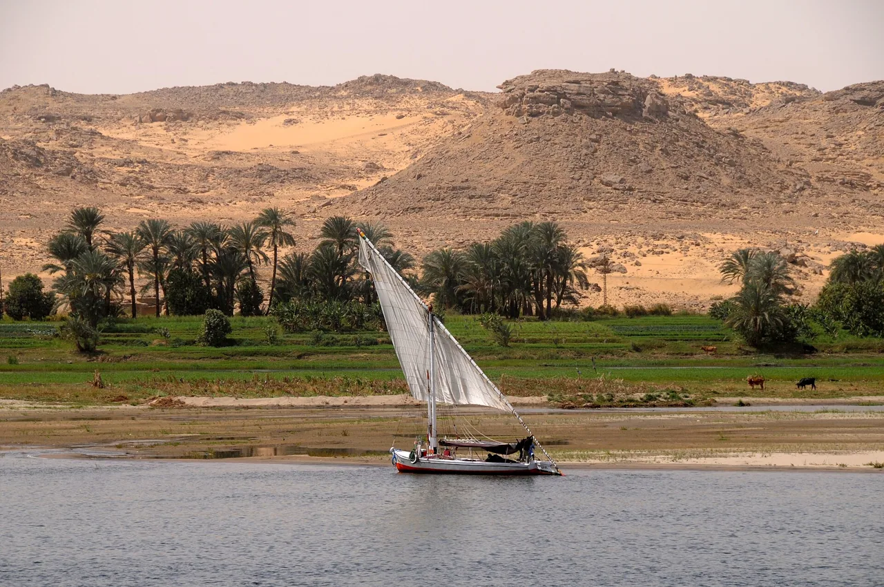 A felucca under sail past green fields and desert hills on the Nile in Upper Egypt