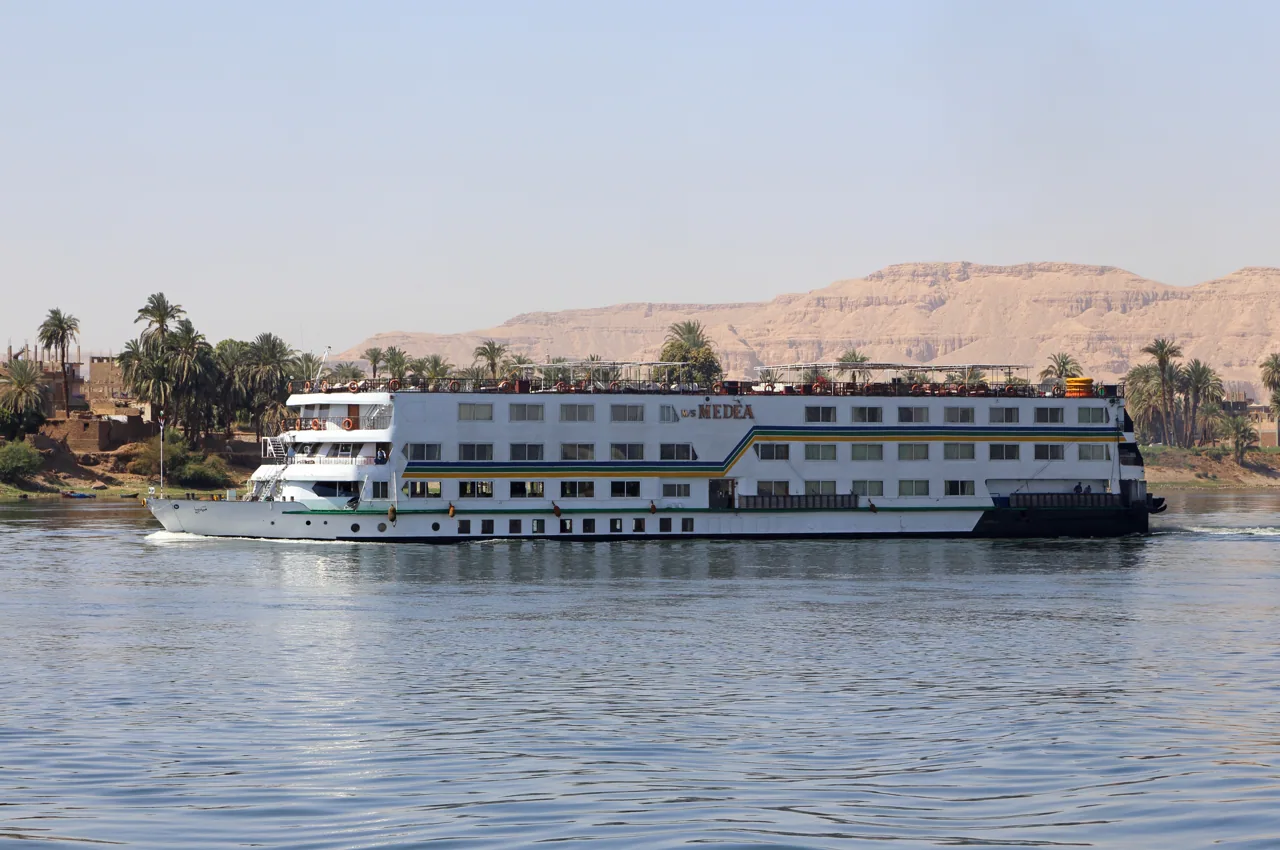 A Nile cruise ship sailing past palm groves with the desert hills of the West Bank behind