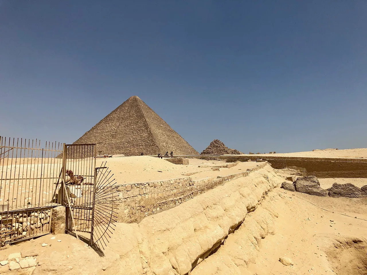 The Great Pyramid of Giza behind excavated walls and an iron gate on the plateau